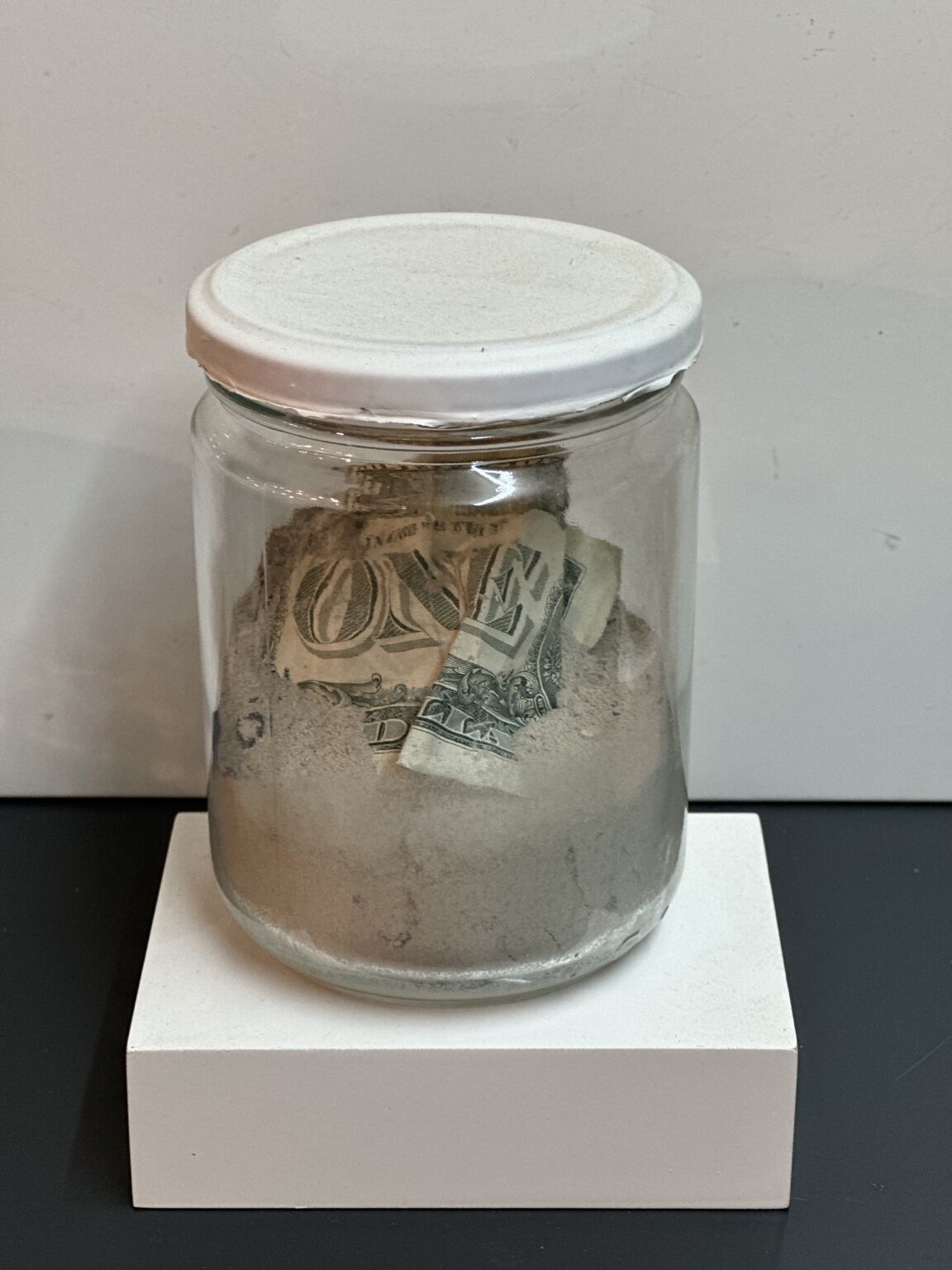 Instalación de cenizas by José Cosme, glass vessel containing ashes and fragments of a banknote